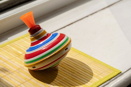 Colorful striped spinning top toy near a window in sunlight, vintage retro children's toy, classic mechanical toys symbol, traditional games, fun, nostalgic childhood toys concept, nobody, closeupの写真素材