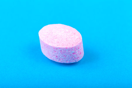 Macro extreme closeup of a single pink purple candy sugar tablet resembling a medicine pill isolated on vibrant blue background, colorful sweet lozenge minimal composition with copy space, sugar pillsの写真素材