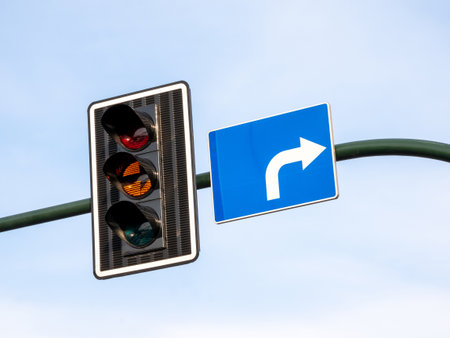 Closeup of an amber traffic light illuminated orange signal next to blue right turn road sign, urban street intersection waiting, caution, driving regulations, laws, transportation direction conceptの写真素材