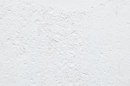 Thick layers of bright white cracked glossy paint on a wall, old rough crackle texture of aged coating with fissures and flaking chips, abstract grunge background surface, material structure closeupの写真素材