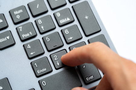 Closeup macro view of human hand pressing number two key on numeric keypad of a computer keyboard, office data entry concept, finger interacting with numpad buttons accounting job work calculationsの写真素材