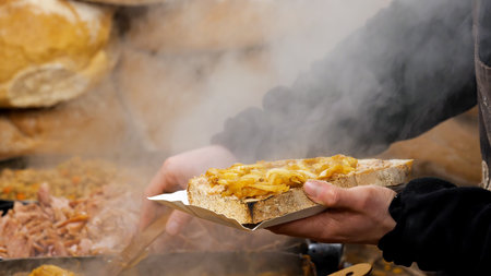 Steaming slice of rustic bread topped with caramelized onions at a street food festival, vendor hands serving a hot savory snack on a paper tray, traditional comfort cuisine at an outdoor marketの写真素材