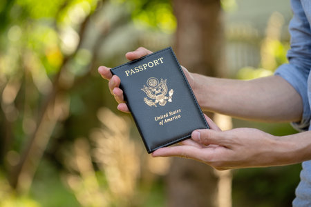 Male hands presenting a United States of America USA passport book outdoors holding it in hands travel visa and citizenship concept blurred green background copy space, one personの写真素材