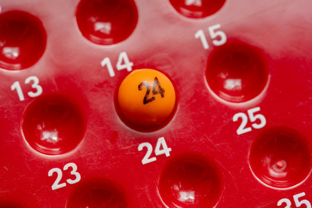 Macro closeup of an orange lottery ball number 24 placed on red bingo game board with numbered slots, concept of luck, chance, random selection, probability and number picking in gaming or gamblingの写真素材
