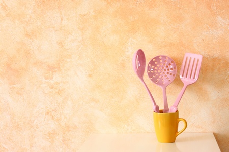 Kitchen cooking utensils  plastic spatulas in yellow cup against rustic terracotta wall の写真素材