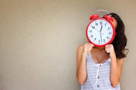 young woman holding clock front of head against a textured wallの写真素材