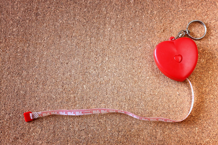 Measuring tape in heart roll over corkboard  good for health or fittness concept  room for text の写真素材
