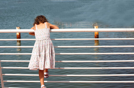 young child standing near fence at sea sideの写真素材