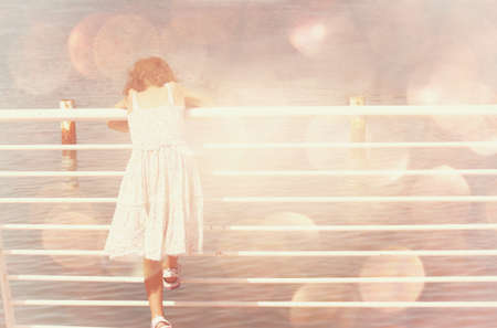 young child standing near fence at sea side  dreamy bokeh lights effectの写真素材