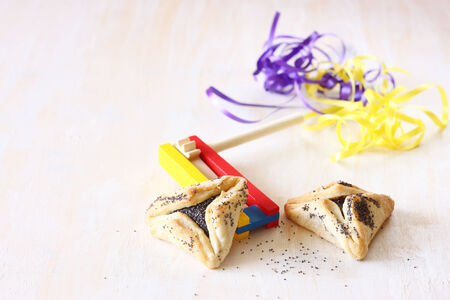 Hamantaschen cookies or hamans ears for Purim celebration and noisemaker over textured wooden boardの写真素材
