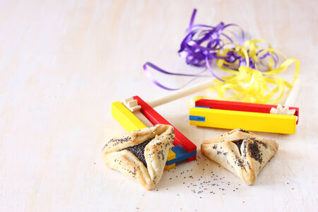 Hamantaschen cookies or hamans ears for Purim celebration and noisemaker over textured wooden boardの写真素材