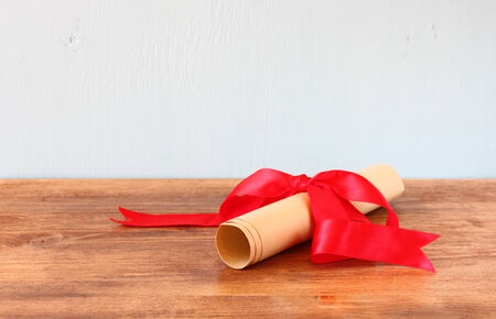 diploma scroll and red ribbon over wooden shelf  の写真素材