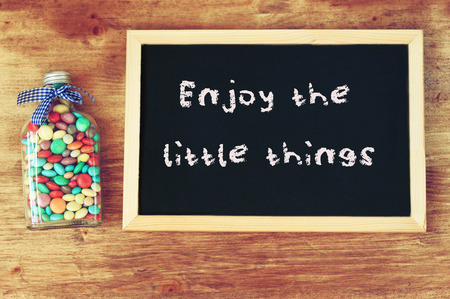 bottle filled with candies and blackboard with the phrase enjoy the little things   の写真素材