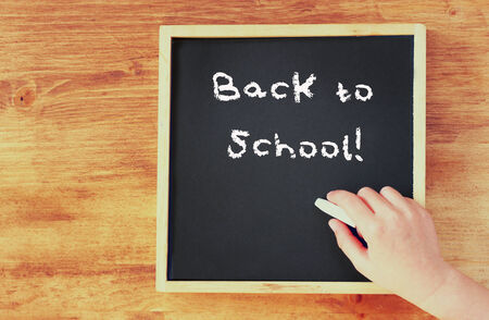 kid hand holding chalk over blackboard with the phrase back to school written on it   の写真素材
