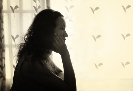 young woman sitting near window and dreaming. retro filtered image. photograph with natural window lightの写真素材