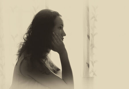 young woman sitting near window and dreaming. retro filtered image. photograph with natural window lightの写真素材