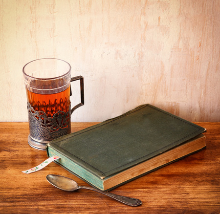 vintage tea glass-holder with fresh lemons and old book over wooden table. retro filtered imageの写真素材