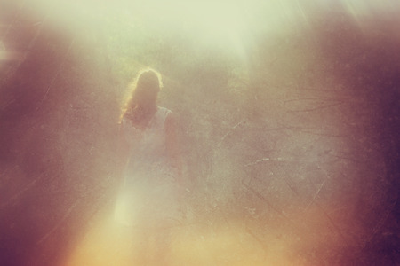 surreal blurred background of young woman stands in forest. abstract and dreamy concept. image is textured and retro tonedの写真素材