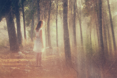 surreal blurred background of young woman stands in forest. abstract and dreamy concept. image is textured and retro tonedの写真素材