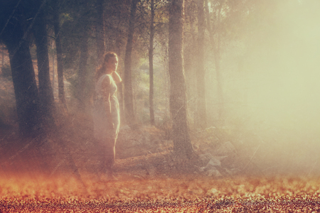 surreal blurred background of young woman stands in forest. abstract and dreamy concept. image is textured and retro tonedの写真素材