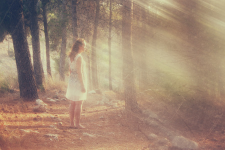 surreal blurred background of young woman stands in forest. abstract and dreamy concept. image is textured and retro tonedの写真素材