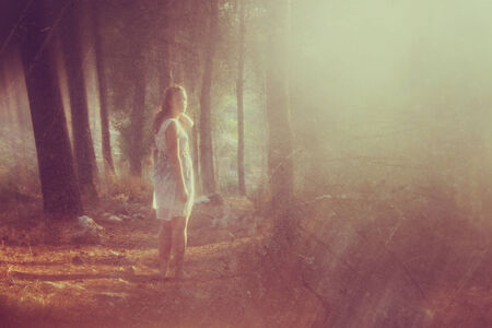 surreal blurred background of young woman stands in forest. abstract and dreamy concept. image is textured and retro tonedの写真素材
