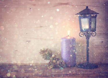 vintage Lantern with burning candles, pine cones on wooden table and glitter lights background. filtered imageの写真素材