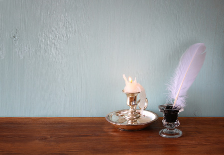 low key image of white Feather, inkwell, and candle on old wooden tableの写真素材