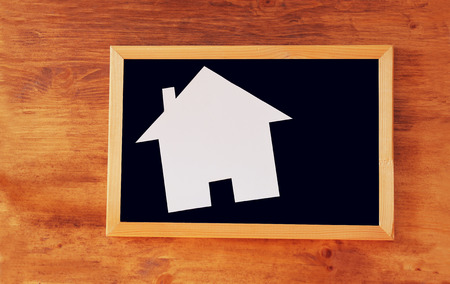 top view of empty blackboard with room for text and house shaped paper cut over wooden tableの写真素材