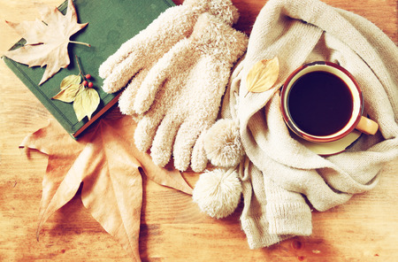 Top view of Cup of black coffee with autumn leaves, a warm scarf and old book on wooden background. filreted imageの写真素材