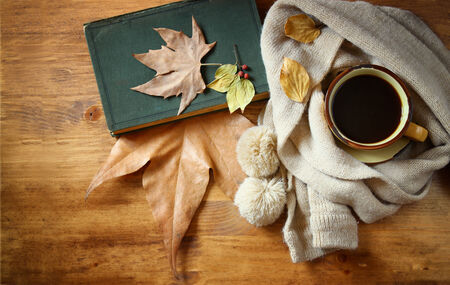 Top view of Cup of black coffee with autumn leaves, a warm scarf and old book on wooden background. filreted imageの写真素材