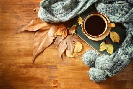 Top view of Cup of black coffee with autumn leaves, a warm scarf and old book on wooden background. filreted imageの写真素材