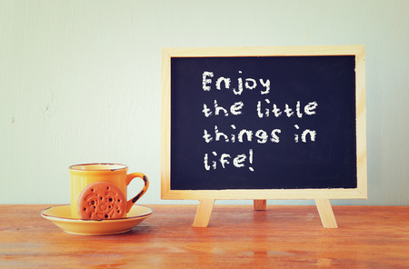 blackboard with the phrase enjoy the little things in life next to coffee cup over wooden tableの写真素材