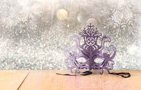 Mysterious Venetian masquerade mask on wooden table and glitter background with snowflake overlaysの写真素材
