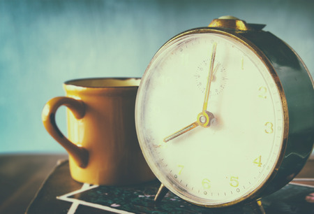 close up image of old clock and cofee cup over wooden table. image is filtered with retro faded styleの写真素材