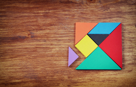 top view of a missing piece in a square tangram puzzle, over wooden table.