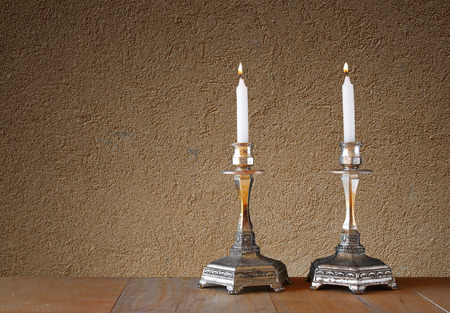 two candlesticks with burning candles over wooden table and textured wall backgroundの写真素材