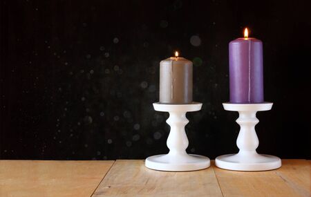 image of Burning candle on wooden table and black textured background