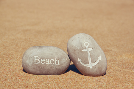 two stone pebbles with the word beach and anchor sign over sandy beachの写真素材