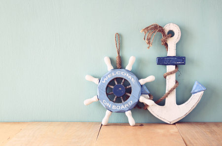 old nautical wood wheel, anchor on wooden table over wooden background. vintage filtered imageの写真素材