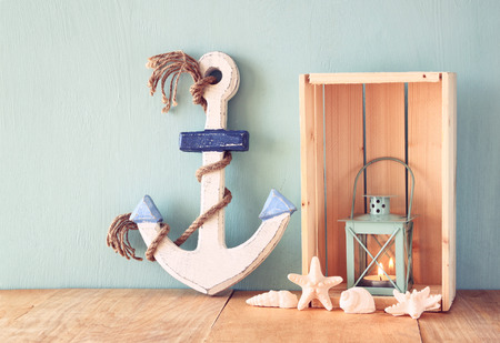 Old nautical wood anchor, lantern and shells on wooden table over wooden aqua backgroundの写真素材