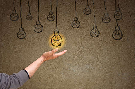 photo of senior man hand and sketch of on and off light bulbs in front of empty textured wall . creativity and solution conceptの写真素材