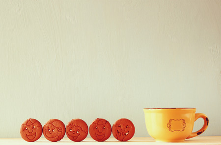raw of cookies with smiley face over wooden table next to cup of coffee. image is retro style filteredの写真素材
