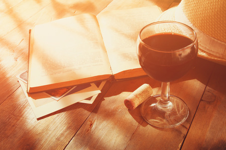 red wine glass and old book on wooden table at sunset burst. vintage filtered imageの写真素材