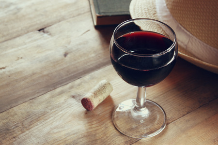 red wine glass and old book on wooden table at sunset burst. vintage filtered imageの写真素材