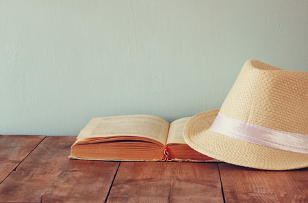 fedora hat and open book over wooden tableの写真素材
