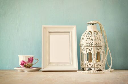 Vintage classical white frame on wooden table with porcelain cup and lanternの写真素材