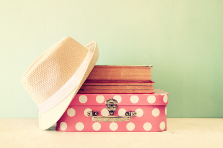photo of pink suitcase with polka dots fedora hat and stack of books over wooden table retro style imageの写真素材