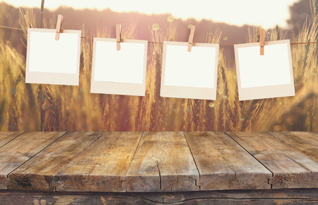 Old  photo frames hanging on a rope with vintage wooden board table in front of wheat field...