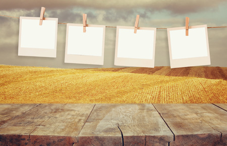 Old  photo frames hanging on a rope with vintage wooden board table in front of wheat field...